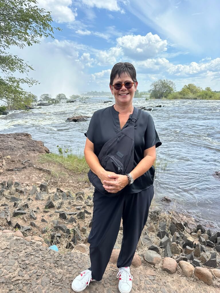 A traveller standing beside the fast-flowing Zambezi River with spray from the falls rising behind